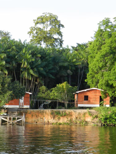 Zwei Holzhütten am Ufer eines Flusses, umgeben von Bäumen