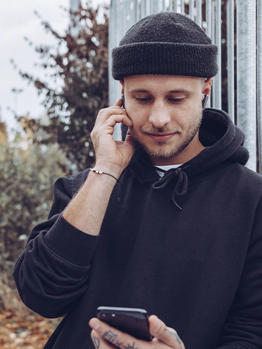 Junger Mann trägt die Hama Bluetooth-Kopfhörer "Spirit Pocket" und bedient sein Handy