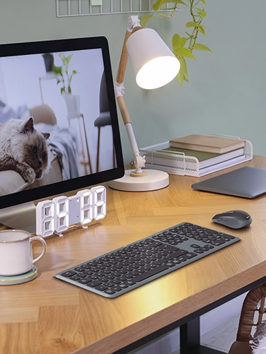 The Hama multi-device keyboard and mouse set ‘WKM-550’, as well as a tablet, floor lamp, digital clock and screen are placed on a wooden desk