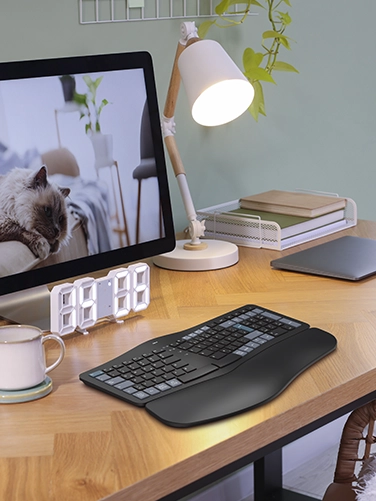 The Hama ‘WK-900 Ergo’ multi-device keyboard, tablet, floor lamp, digital clock and screen are placed on a wooden desk