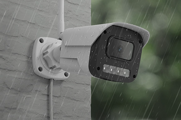 The Hama smart outdoor surveillance camera with Wi-Fi, night vision, 1080p and recording is mounted on a stone wall. You can see that it's raining.