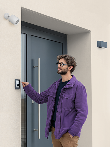 A man rings the doorbell and looks into Hama's smart surveillance camera. 