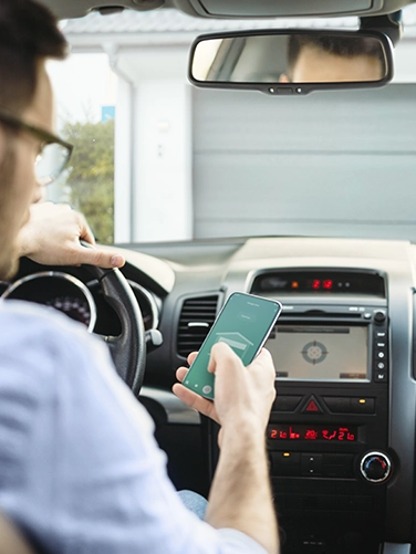Ein Mann sitzt im Auto vor seiner Garage. Mit dem Smartphone in seiner Hand kann er über Smart Home App die Garage automatisch öffnen.